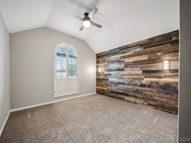 carpeted empty room with ceiling fan, vaulted ceiling, and wood walls