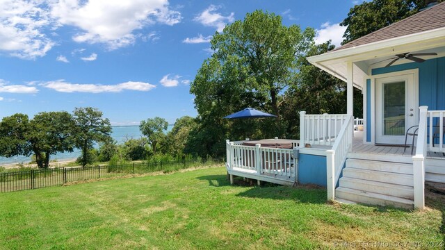 view of yard with a deck with water view and ceiling fan