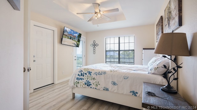 bedroom with ceiling fan, a tray ceiling, and light hardwood / wood-style flooring