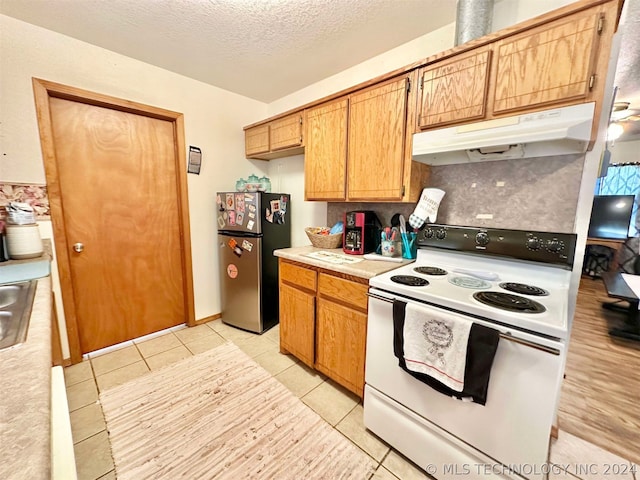 kitchen with sink, stainless steel refrigerator, light tile patterned floors, a textured ceiling, and electric range