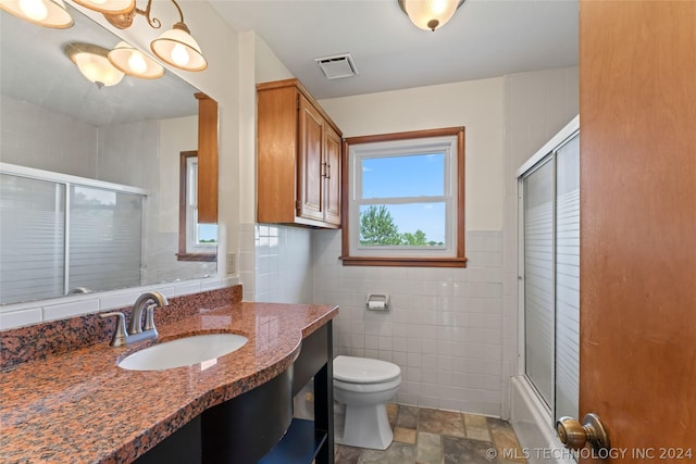 full bathroom with tile walls, toilet, vanity, and shower / bath combination with glass door