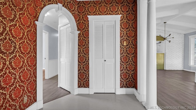 corridor with lofted ceiling with beams, dark tile patterned flooring, an inviting chandelier, and decorative columns