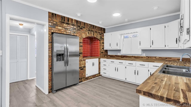 kitchen featuring white cabinetry, stainless steel fridge, butcher block countertops, ornamental molding, and sink