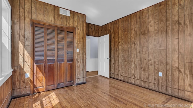 unfurnished bedroom featuring a closet, wood walls, and hardwood / wood-style flooring