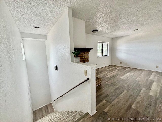 unfurnished living room with visible vents, a textured wall, a textured ceiling, and wood finished floors