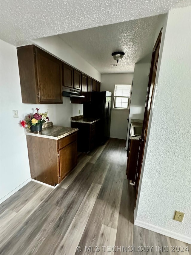 kitchen featuring dark brown cabinetry, black refrigerator, light hardwood / wood-style flooring, and a textured ceiling