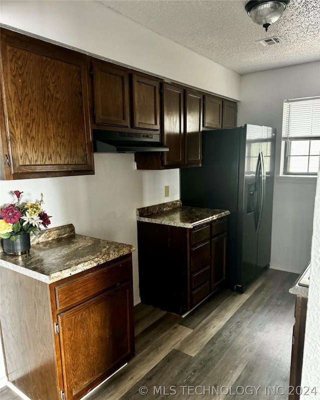 kitchen with a textured ceiling, dark hardwood / wood-style floors, black fridge, and dark brown cabinetry