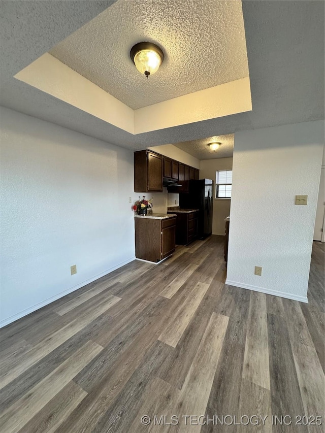 kitchen with a raised ceiling, light countertops, dark brown cabinetry, and wood finished floors