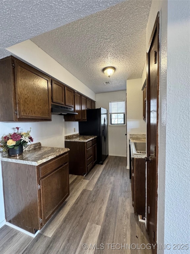 kitchen with dark brown cabinetry, light wood finished floors, light countertops, a textured ceiling, and under cabinet range hood