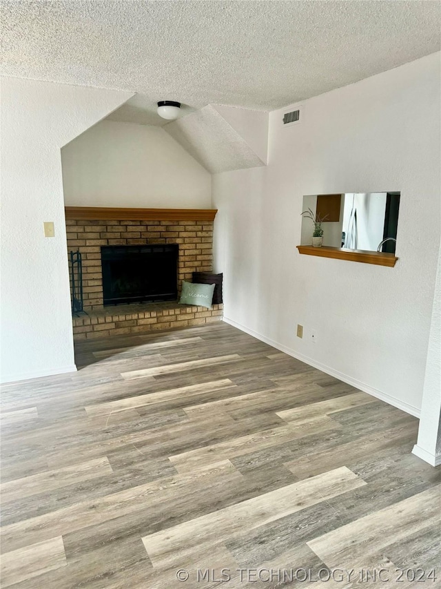 unfurnished living room with a brick fireplace, wood-type flooring, a textured ceiling, and vaulted ceiling