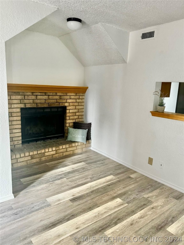 unfurnished living room with a textured ceiling, a brick fireplace, lofted ceiling, and hardwood / wood-style floors