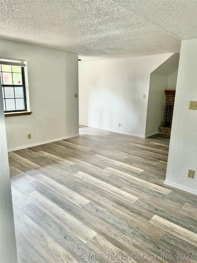 unfurnished room featuring a textured ceiling, a brick fireplace, and hardwood / wood-style floors