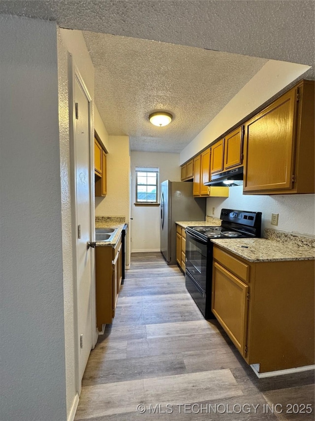 kitchen with a textured ceiling, light wood-style flooring, under cabinet range hood, black electric range oven, and brown cabinetry