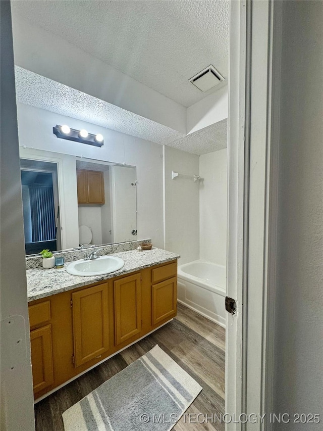 bathroom with wood finished floors, a textured ceiling, vanity, shower / bath combination, and visible vents