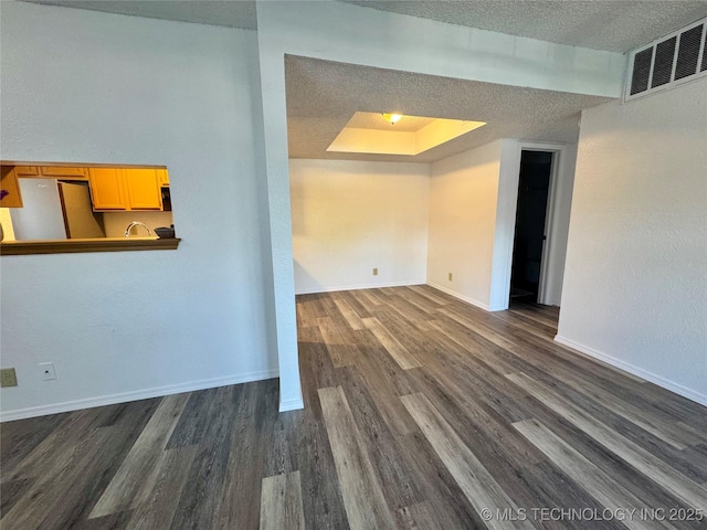 spare room featuring a textured ceiling, a raised ceiling, baseboards, dark wood-style flooring, and visible vents