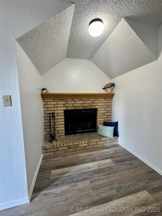 unfurnished living room featuring wood finished floors, a textured ceiling, baseboards, lofted ceiling, and a brick fireplace