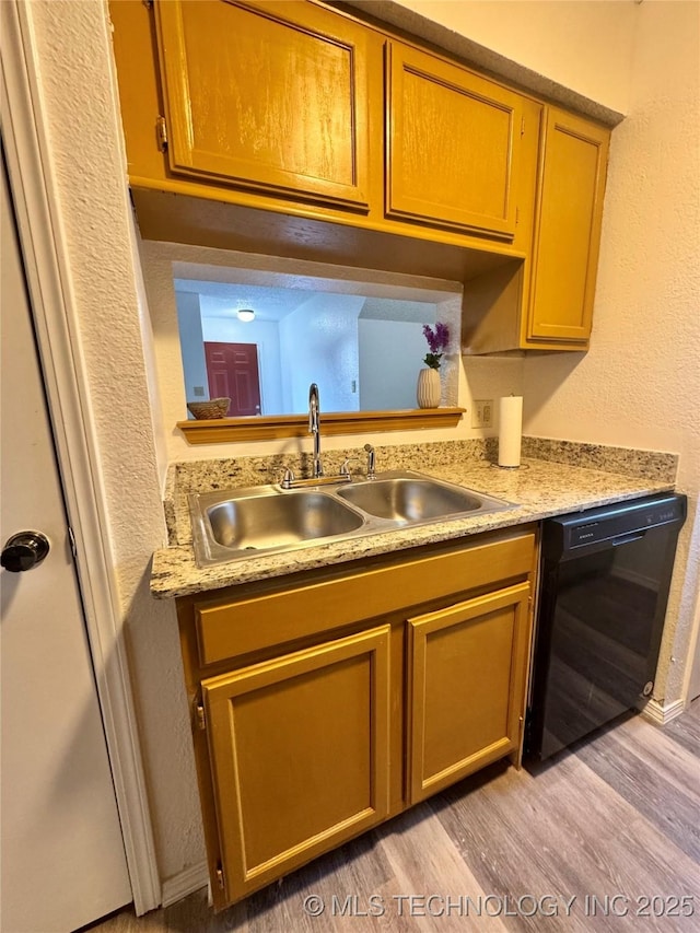 kitchen with light wood finished floors, light countertops, a sink, and black dishwasher