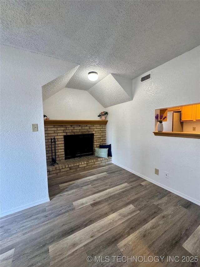 unfurnished living room with wood finished floors, visible vents, baseboards, a fireplace, and a textured ceiling