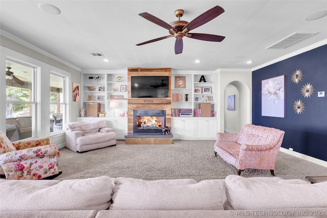 carpeted living room with built in features, ceiling fan, a multi sided fireplace, and crown molding