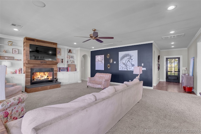 living room with a large fireplace, ceiling fan, built in shelves, crown molding, and light hardwood / wood-style flooring