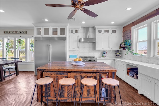 kitchen featuring a wealth of natural light, built in fridge, tasteful backsplash, and wall chimney exhaust hood