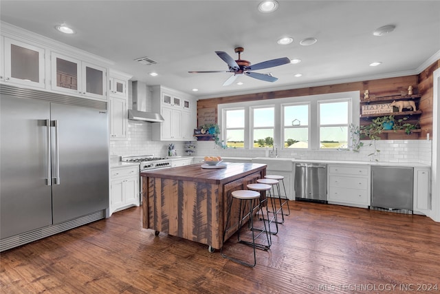 kitchen with white cabinetry, dark wood-type flooring, backsplash, wall chimney exhaust hood, and high end appliances