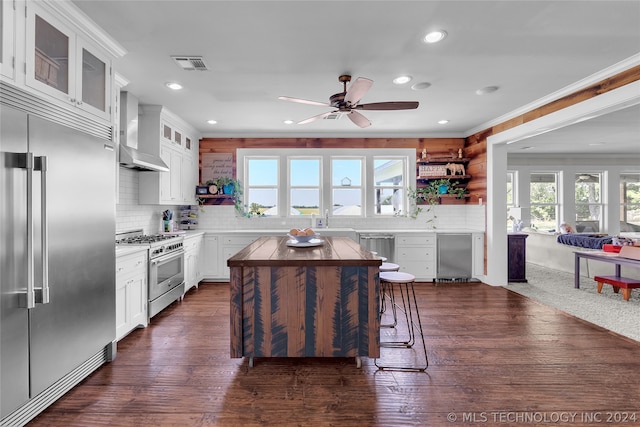 kitchen featuring plenty of natural light, backsplash, high end appliances, and wall chimney range hood