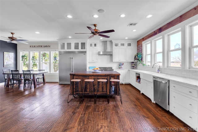 kitchen with wall chimney range hood, appliances with stainless steel finishes, dark hardwood / wood-style floors, and a healthy amount of sunlight