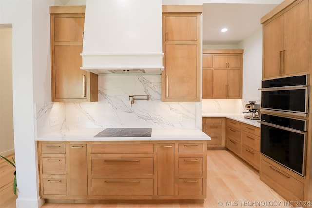 kitchen with backsplash, premium range hood, black appliances, and light wood-type flooring