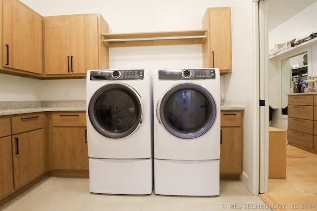 washroom featuring separate washer and dryer, cabinets, and light wood-type flooring