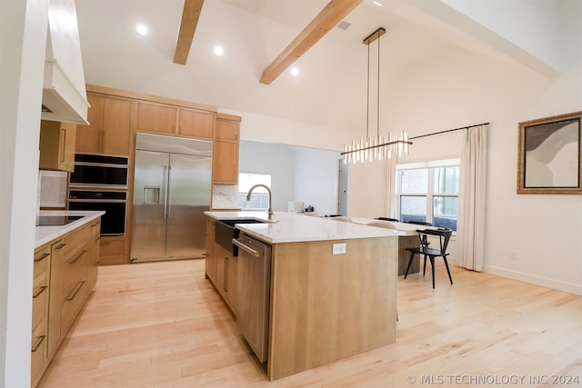 kitchen featuring light hardwood / wood-style flooring, stainless steel appliances, an island with sink, hanging light fixtures, and beam ceiling