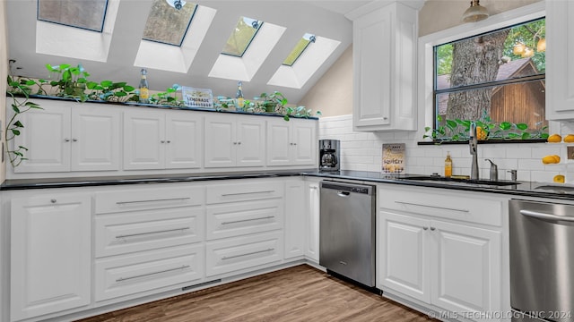 kitchen featuring sink, dishwasher, white cabinets, and vaulted ceiling with skylight