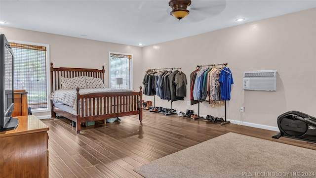 bedroom featuring ceiling fan, dark wood-type flooring, multiple windows, and a wall unit AC