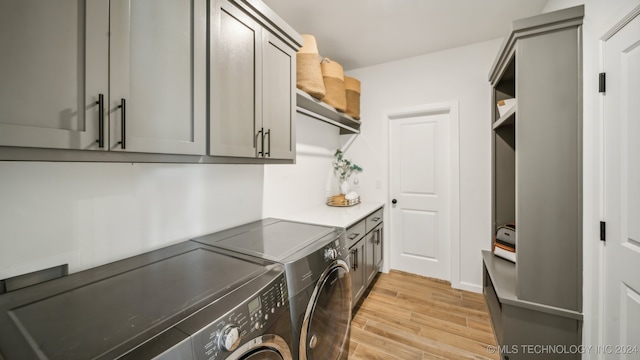 washroom featuring washing machine and dryer, cabinets, and light wood-type flooring