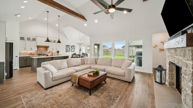 living room with ceiling fan with notable chandelier, a fireplace, beam ceiling, high vaulted ceiling, and light hardwood / wood-style flooring