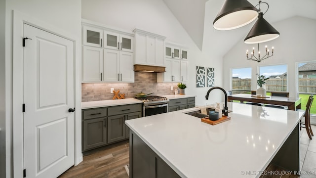 kitchen featuring white cabinetry, a kitchen island with sink, sink, stainless steel range with gas cooktop, and decorative light fixtures