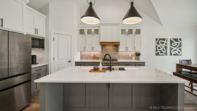 kitchen featuring stainless steel appliances, vaulted ceiling, decorative light fixtures, white cabinets, and a center island with sink