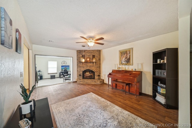 living room featuring wood-type flooring, a brick fireplace, ceiling fan, and a textured ceiling