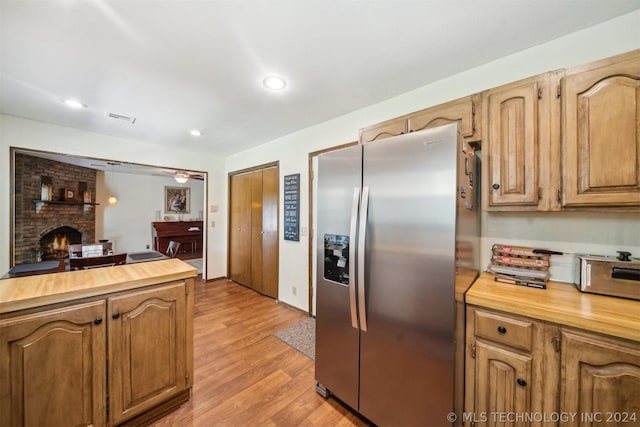 kitchen featuring a fireplace, butcher block counters, stainless steel fridge with ice dispenser, and light hardwood / wood-style flooring