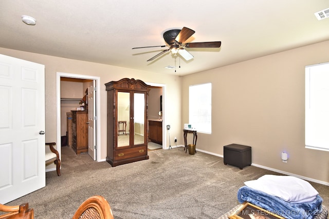 carpeted bedroom with multiple windows, connected bathroom, a walk in closet, and ceiling fan