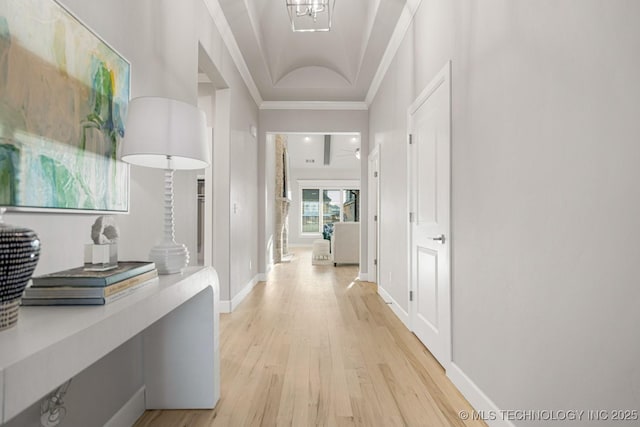 hall featuring light wood-style flooring, ornamental molding, and baseboards