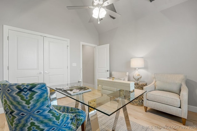 living area with high vaulted ceiling, light wood finished floors, a ceiling fan, and baseboards