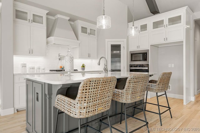 kitchen featuring wall oven, light wood finished floors, built in microwave, premium range hood, and a sink