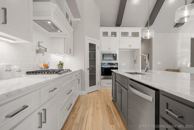 kitchen featuring light stone counters, glass insert cabinets, custom exhaust hood, stainless steel appliances, and a sink