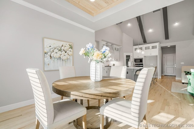 dining space featuring lofted ceiling with beams, crown molding, light wood-type flooring, and baseboards