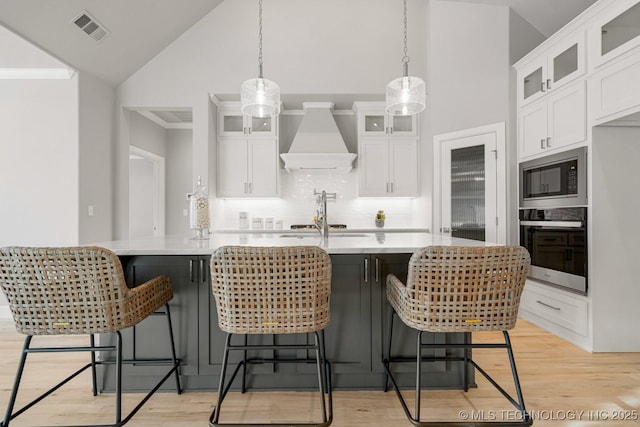 kitchen with visible vents, white cabinets, built in microwave, oven, and premium range hood