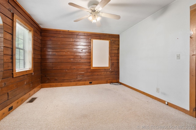 empty room with carpet floors, wood walls, and ceiling fan