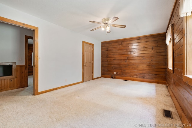 carpeted spare room featuring wood walls and ceiling fan