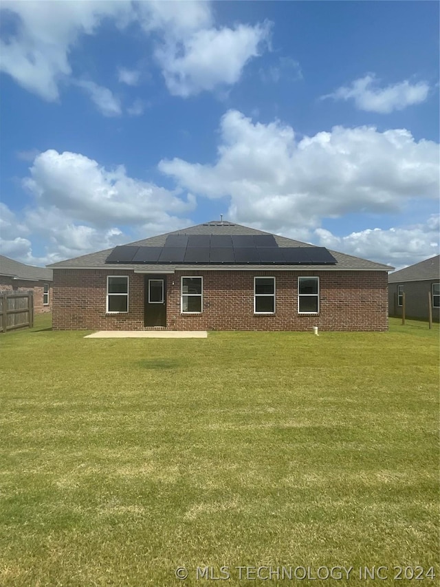 rear view of house featuring a yard and solar panels