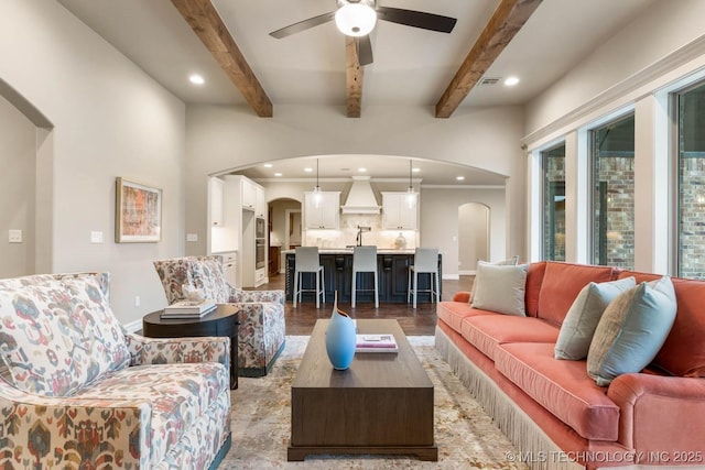 living room with beamed ceiling, ceiling fan, ornamental molding, and dark hardwood / wood-style floors